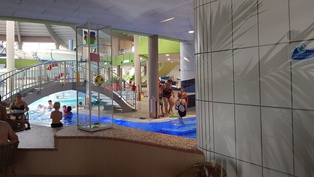 Une piscine intérieure dotée d’un espace clos par des parois de verre, d’un toboggan aquatique et d’un escalier menant à un niveau supérieur.