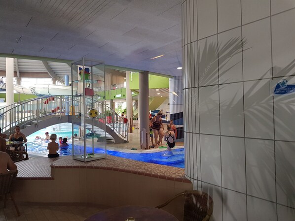 An indoor swimming pool with a glass-enclosed area, a water slide, and a staircase leading to a higher level.