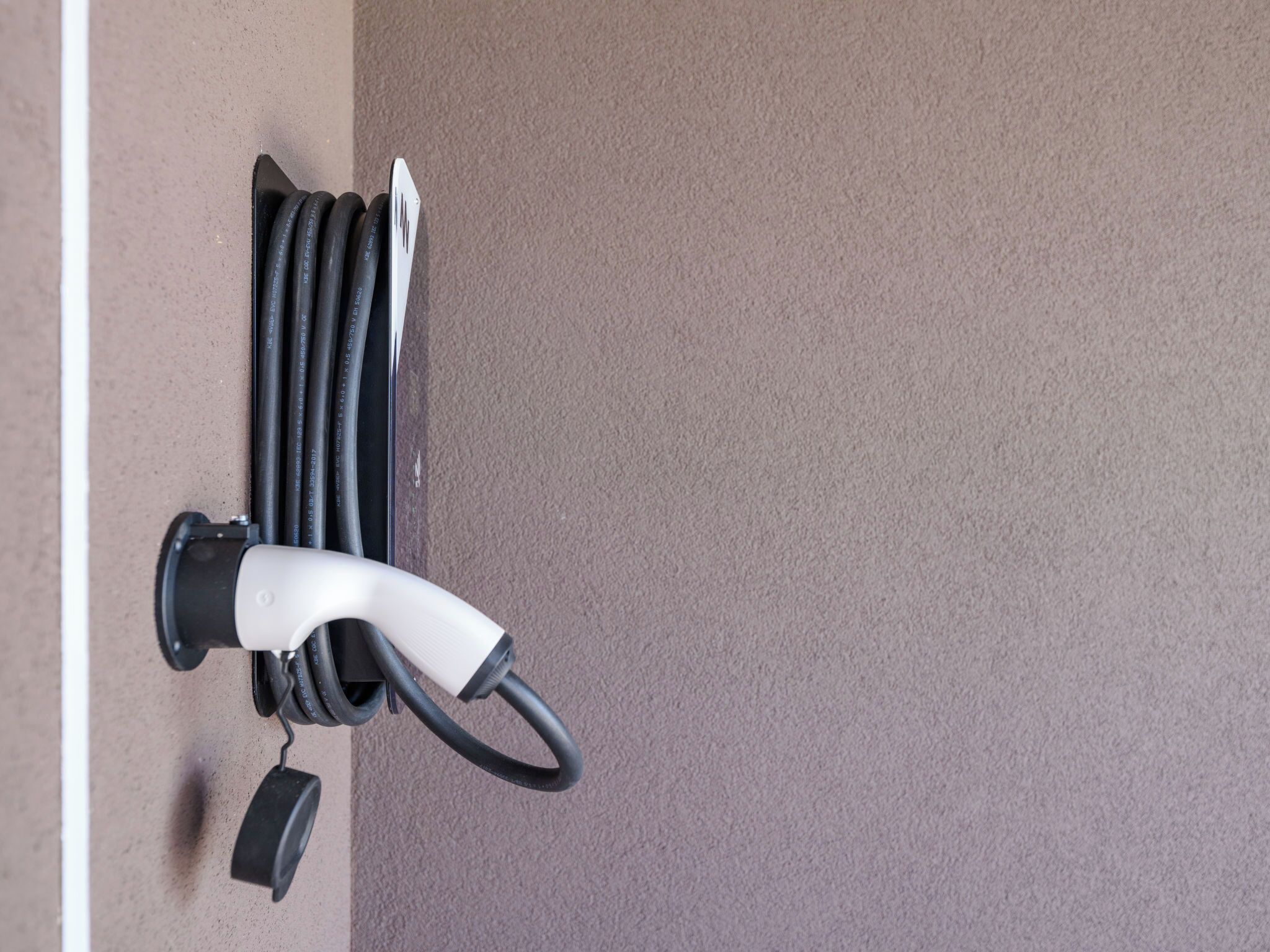 Estació de càrrega elèctrica per a vehicles instal·lada a la paret, amb cable i endoll.
