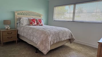 Un dormitorio con cama, mesita de noche, lámpara y ventana con persianas.