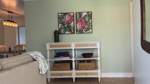 Un salon comprenant un canapé, une console blanche agrémentée de paniers et deux œuvres d’art florales encadrées accrochées au mur.