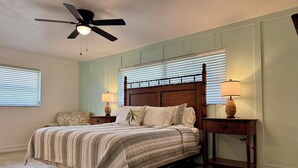 A bedroom with a bed, two bedside tables with lamps, a ceiling fan, and a window with blinds.