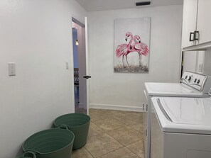 Ein Waschraum mit einer weißen Waschmaschine, grünen Eimern und einem Flamingo-Gemälde an der Wand.