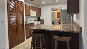 A kitchen with wooden cabinets, a microwave, stove, and bar stools.