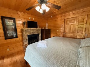 A wooden cabin room with a stone fireplace, a bed, a television, and a ceiling fan. - 3 bedroom cabin near Dollywood.  Mountain views, hot tub, games, community pool. (Sevierville)