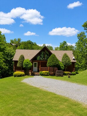 A log cabin with a gravel driveway, surrounded by lush greenery and trees. - 3 bedroom cabin near Dollywood.  Mountain views, hot tub, games, community pool. (Sevierville)