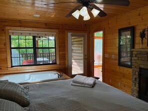 Ein Zimmer in einer Holzhütte mit Badewanne, einem Bett, einem Deckenventilator und einem Kamin.