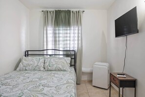 A bedroom with a bed, a television, a small table, and a window with curtains. - Cozy 3BR Condo Pool  10 minutes to Airport (Carolina)