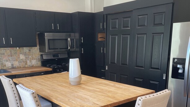 A modern kitchen with a wooden island, black cabinets, stainless steel appliances, and two upholstered chairs.