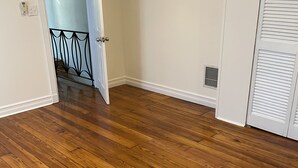 A room with wooden flooring, white walls, and a door leading to a staircase.