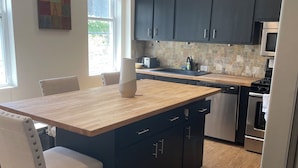 A modern kitchen with dark cabinets, a wooden island, and a dining area with a chair.