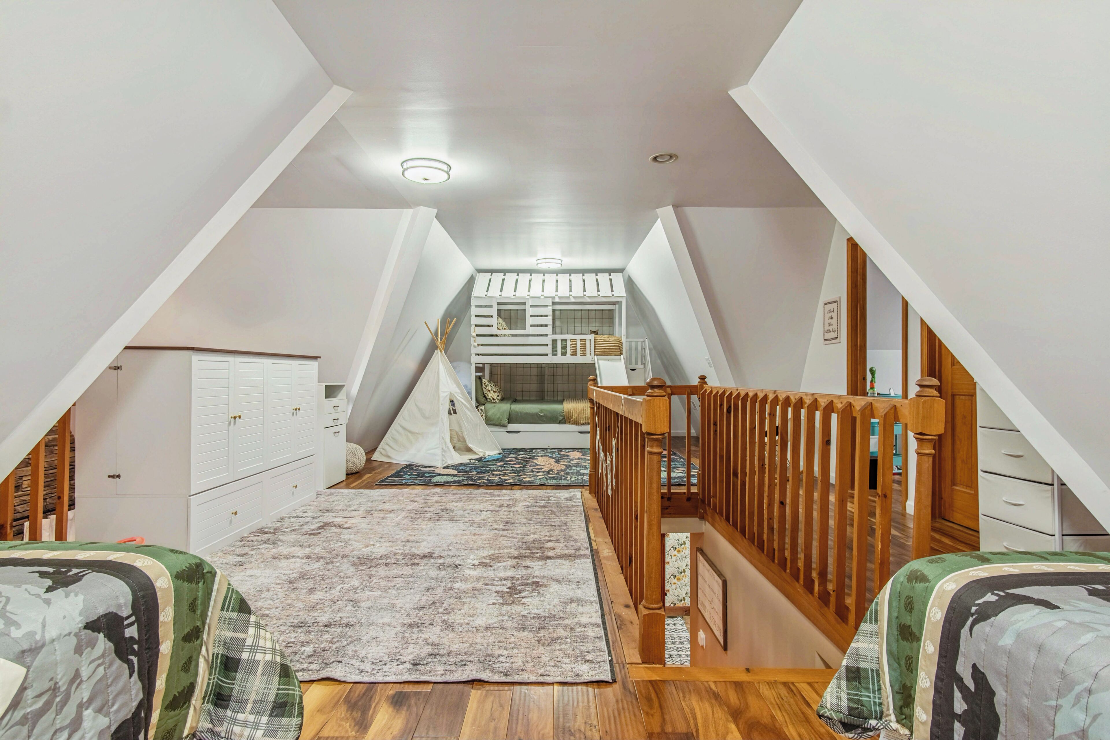 A loft bedroom with a sloped ceiling, a wooden staircase, a bunk bed, and a small kitchenette.