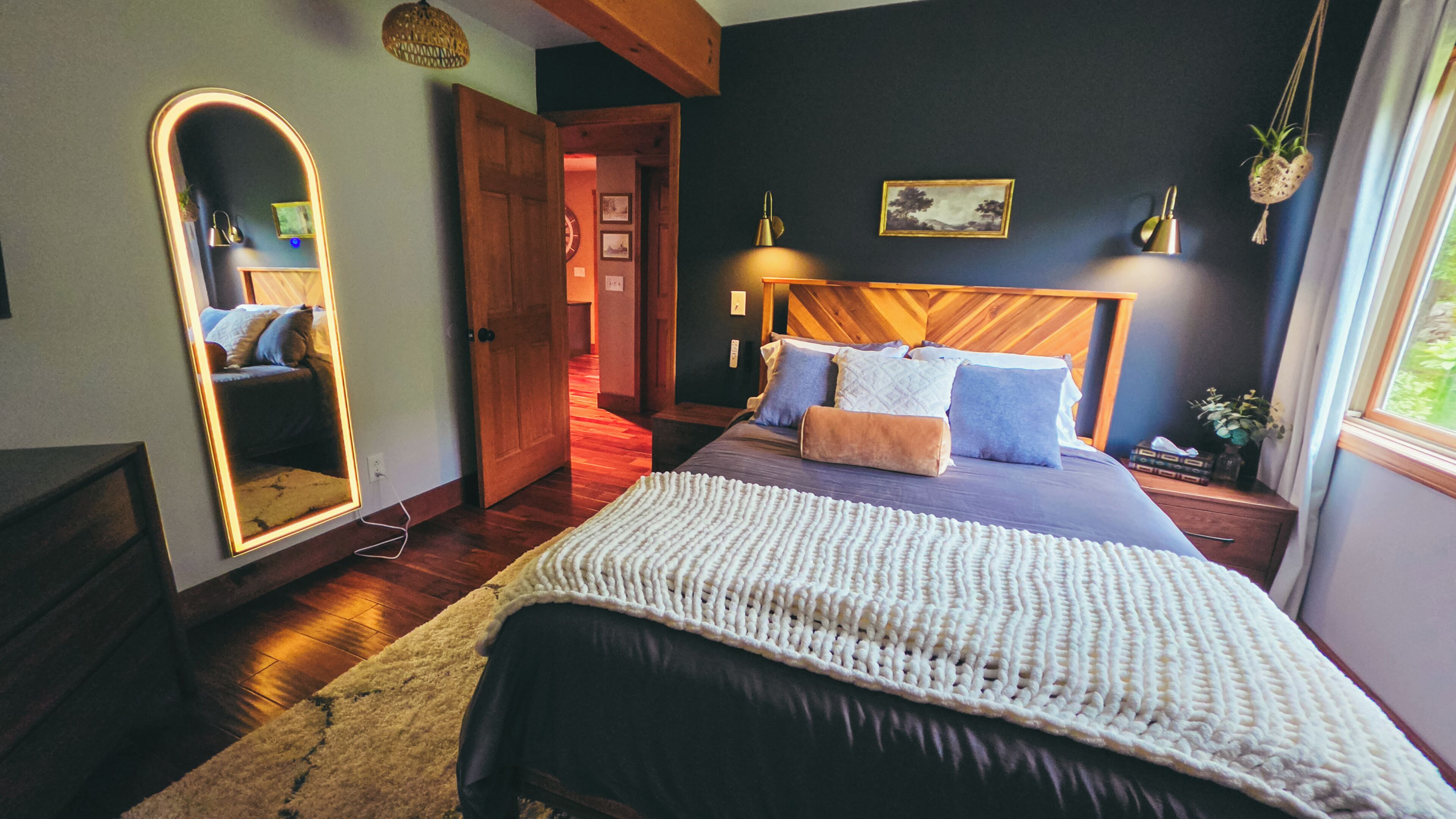 Un dormitorio con cama, espejo, cabecero de madera, mesita de noche y ventana.
