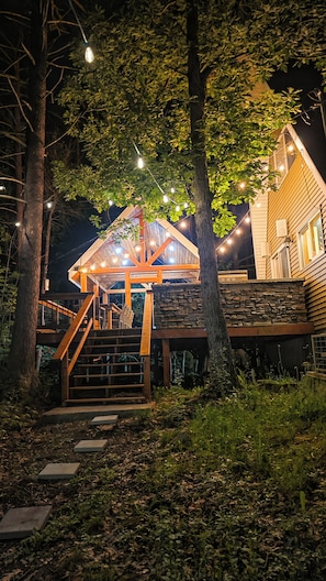 Une cabane en bois avec des fondations en pierre, une terrasse en bois et un escalier menant à l’entrée.