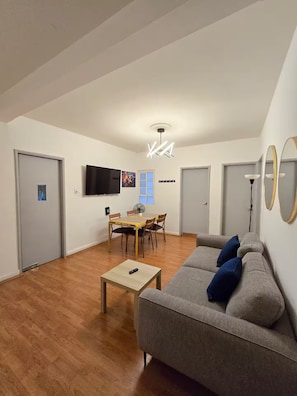 Ein modernes Wohnzimmer mit einem grauen Sofa, einem Holztisch und einem Essbereich mit Stühlen und Tisch.