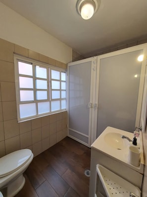 Ein Badezimmer mit Toilette, einem Fenster mit Milchglas, einer Duschkabine und einem Waschbecken mit Spiegel.