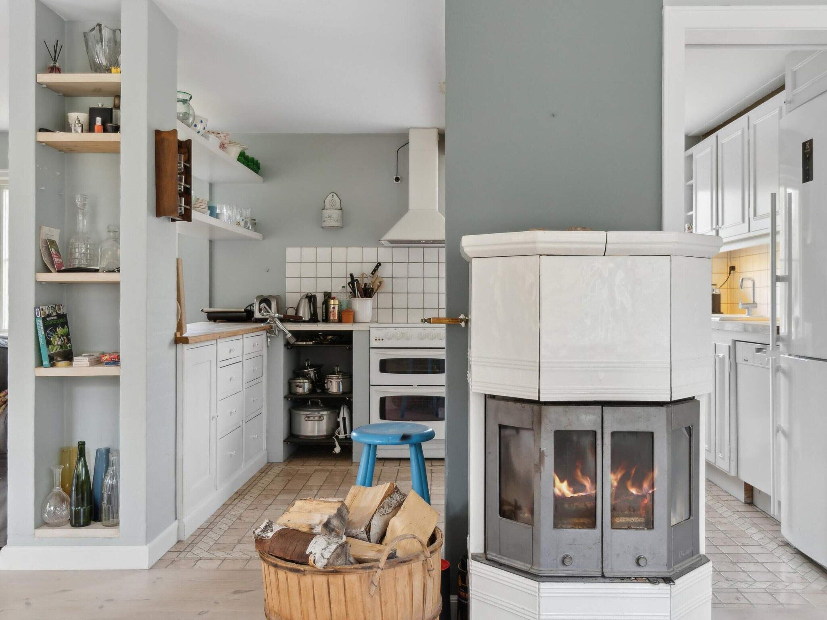 Een moderne keuken met witte kasten, een centraal eiland, een fornuis met vlammen en een blauwe kruk.