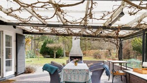 Un patio al aire libre con mobiliario de mimbre, una mesa con mantel floreado y una chimenea de ladrillo.