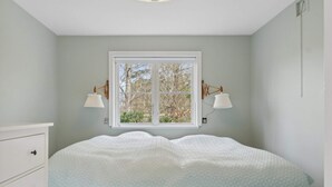 Un dormitorio con una cama, dos lámparas de noche, una ventana y un aparador blanco.