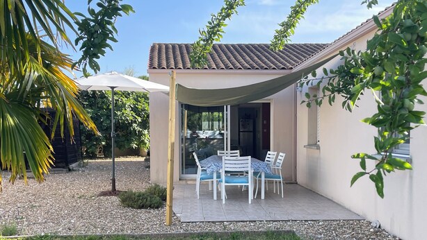 Eine Terrasse mit Tisch und Stühlen, ein überdachter Bereich und ein Gebäude mit Ziegeldach.