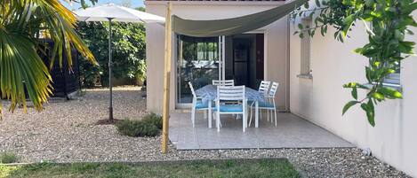 A patio with a table and chairs, a covered area, and a building with a tiled roof.