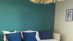 Ein Bett mit weißer Bettwäsche, blauen Kissen und einer Hängeleuchte aus gewebtem Material.