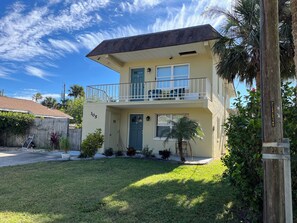 A two-story building with a balcony, a front door, and a small front yard with a palm tree. - NEW!  Jasmine Beach Loft - 2 Blocks to Ocean! (Flagler Beach)