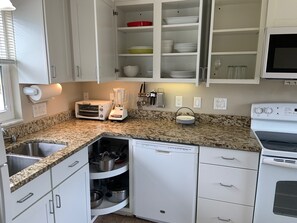 Eine Küche mit weißen Schränken, einer Granit-Arbeitsplatte, einem Toaster, einem Mixer, einer Spülmaschine und einem Herd.