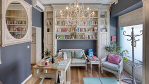 A room with a large bookcase, a chandelier, a sofa, and a table with books and decorative items. - Cosy studio, large balcony, shared terrace GOTWN7 (Sliema)
