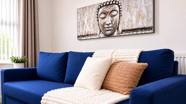 Ein blaues Sofa mit einer weißen und braunen Decke, ein Buddha-Gemälde zur Dekoration und ein Blumentopf.