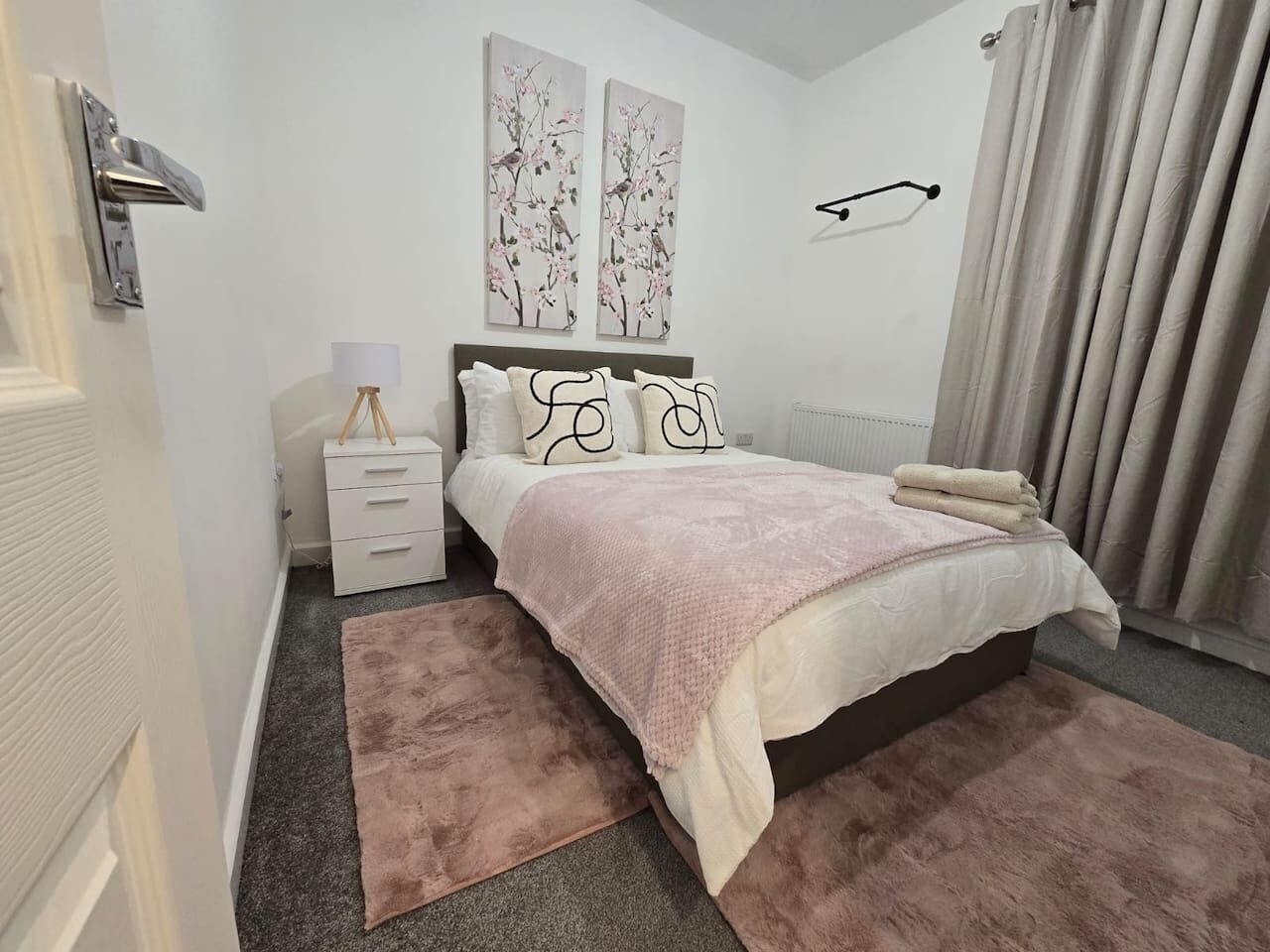 A bedroom with a bed, bedside table, lamp, and artwork on the wall.