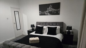 Ein Schlafzimmer mit einem Bett, zwei Nachttischen, einem Schreibtisch und einem großen Fenster sowie einer Tür.