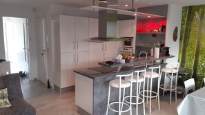 A modern kitchen with white cabinets, a central island with bar stools, and a red-lit bar area. - Beautiful 3-bedroom apartment (70 square meters) in Juan (Antibes)