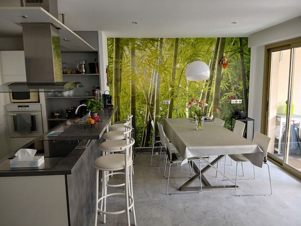 A modern kitchen with a dining area, featuring a kitchen island, bar stools, and a table with a vase of flowers. - Beautiful 3-bedroom apartment (70 square meters) in Juan (Antibes)