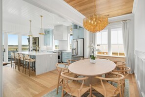 A spacious kitchen with a central island, wooden bar stools, and a dining table with chairs. - LUXURY 5 BR WATERFRONT RETREAT ON EDISTO BEACH W/ PRIVATE POOL & DEEPWATER DOCK (Edisto Island)