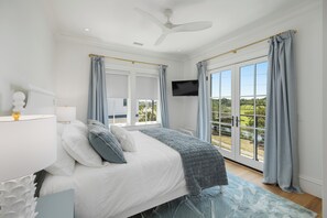 Ein Schlafzimmer mit Bett, Deckenventilator, Fernseher und einem Balkon mit Vorhängen.