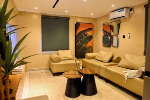 A modern living room with a sofa, two round tables, a large mirror, and a potted plant.