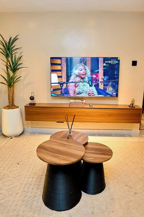 A modern hotel lobby with a flat-screen TV, a wooden reception desk, a potted plant, and a round dining table with black legs.