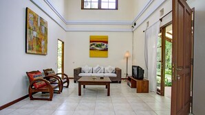 Un salon comprenant un canapé, des fauteuils, une table basse, un téléviseur et des œuvres d’art accrochées aux murs.