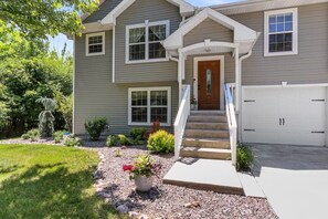 A two-story house with a front porch, a garage, and a garden with various plants and a potted flower.