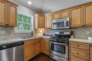 A kitchen with wooden cabinets, a stainless steel dishwasher, a microwave, a stove, and a window with a view of greenery.