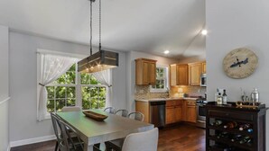 Une cuisine moderne avec des meubles en bois, une table à manger avec des chaises, un meuble à vin et une horloge au mur.