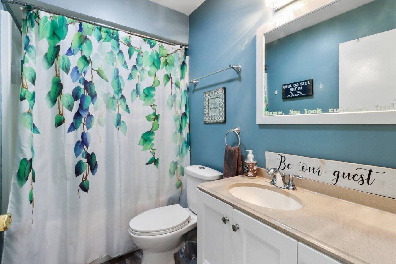 Une salle de bain avec un rideau de douche, des toilettes, un lavabo et un miroir sur lequel est inscrit : « Soyez les bienvenus ».
