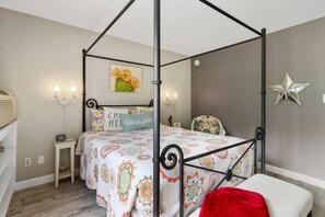 Een hemelbed met een bed met patroon, een nachtkastje met een lamp, een stoel en een muur met een ster decoratie en een lijst met een afbeelding.
