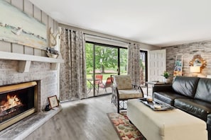 A living room with a fireplace, a sofa, a coffee table, and a view of the outdoors.