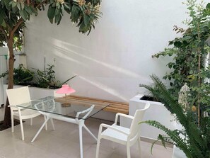 Ett bord med glasskiva och vita stolar, en rosa lampa och växter i en modern utomhusmiljö.