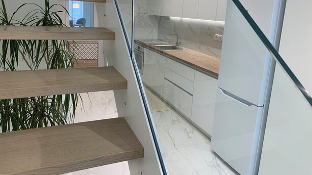 Una cocina moderna con salpicadero de mármol, estanterías de madera y un refrigerador empotrado.