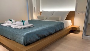 Un dormitorio moderno con una cama plataforma de madera, ropa de cama blanca y colcha color turquesa.