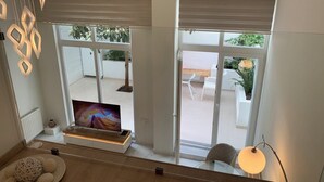 Una sala moderna con televisor, una zona de comedor con sillas y un balcón con plantas.