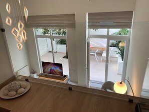 Une chambre moderne avec un téléviseur posé sur un meuble en bois, une porte vitrée donnant sur l’extérieur et un luminaire suspendu.